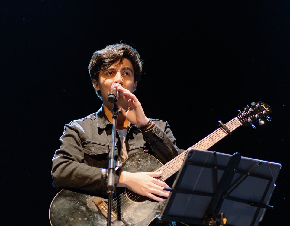 Kike de León canta con su guitarra bajo luz azul en el escenario